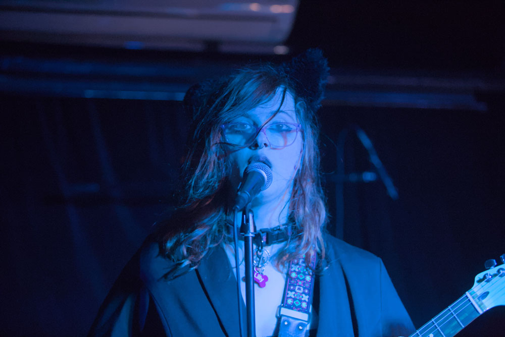 A more close-up photo of the guitarist from the above image, singing into a microphone.