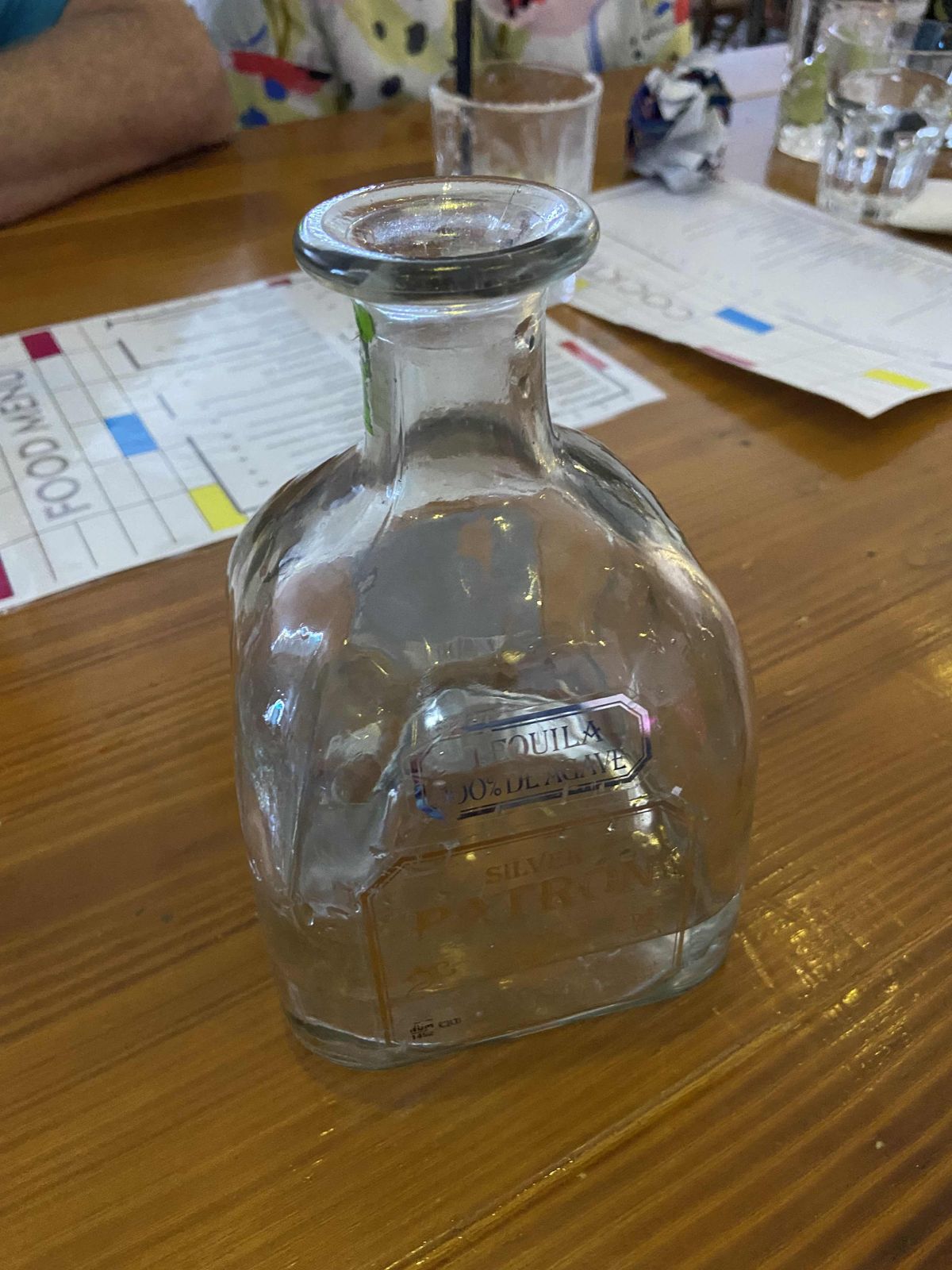 A squat, square glass bottle labelled as Patron silver tequila. The bottle contains water.