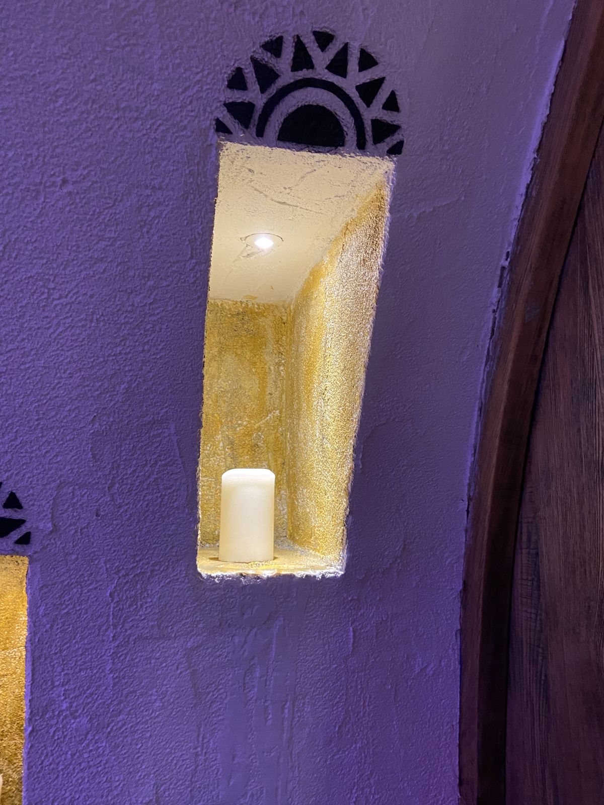 A wall alcove holding a round candle. The candle is unlit, and the alcove is lit by inbuilt electric lighting.
